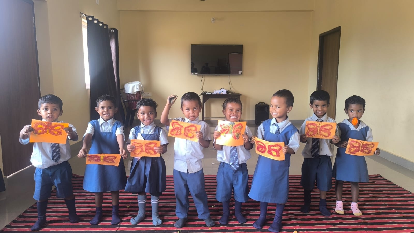 Children in school uniforms holding butterfly artwork